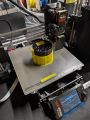 Photo of a black nose cone being printed on a Prusa Mk4 3D printer with yellow supports.