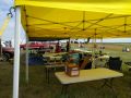 A photo of several tables laden with rockets and rocket equipment, under a large yellow canopy tent.